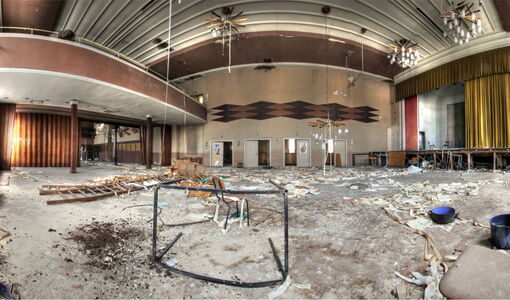 Verlassener Saal mit Bühne und Balkon.